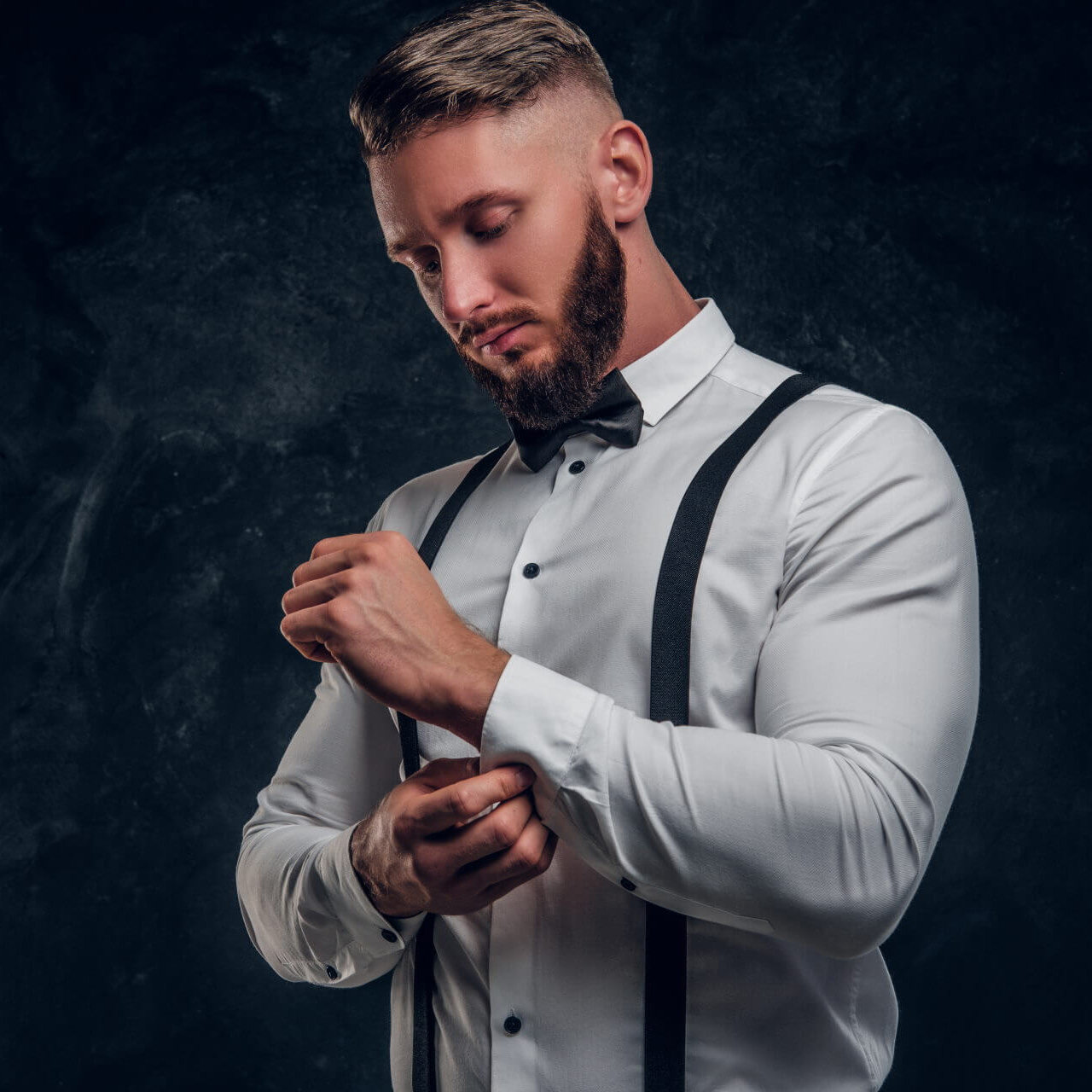 Shutterstock 1364542916 Stattlicher Mann in weißem Hemd mit Hosenträgern welcher sich den linken Hemdsärmel richtet.